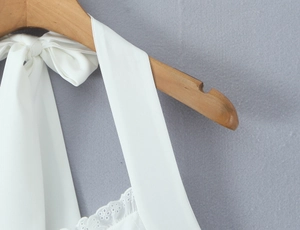 Gros plan d'une robe blanche en mousseline avec broderie ajourée et col licou sur cintre
