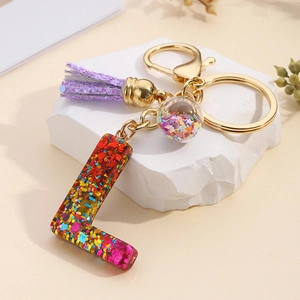 Detail of L-shaped resin keychain with glitter, purple tassel, and golden hardware
