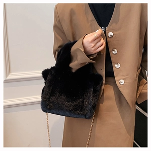 Sac à main en peluche noire avec bandoulière dorée porté par un mannequin en veste