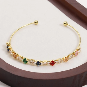 Detail of gold-plated open bangle featuring multi-colored gemstones on white texture
