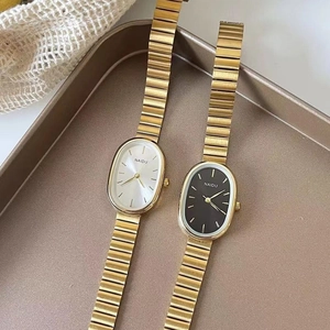 Detailed macro view of oval quartz watches with golden steel bands in a display tray