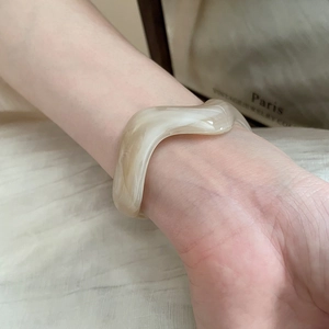 Macro shot of wave-shaped acrylic cuff bracelet with cream marble pattern on wrist