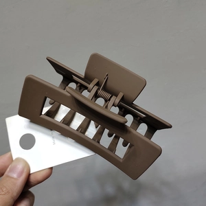 Detail view of large matte brown hair claw clip held by hand against a grey background