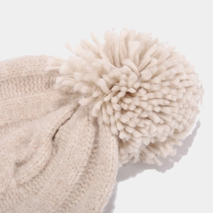 Close-up of a cream cable knit beanie featuring a large pom-pom and thick ribbed texture
