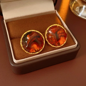 Macro view of amber resin round earrings with gold trim in a brown leather box