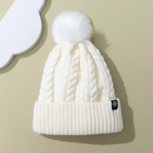 White cable knit beanie with large faux fur pom and snowflake tag for winter warmth