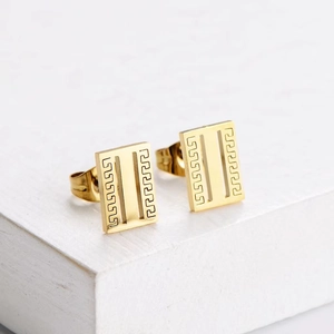 Detail of rectangular gold titanium earrings with classic Greek key pattern on white base