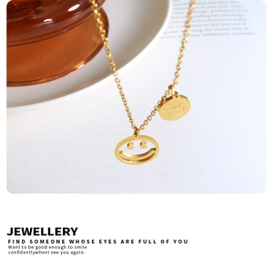 Detalle del collar dorado con colgante de cara sonriente y medalla grabada de Good Luck