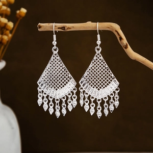 Detailed close-up of ethnic silver leaf tassel earrings on a natural wooden stand