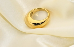 Bague large dorée polie présentée sur un fond élégant en tissu de soie beige