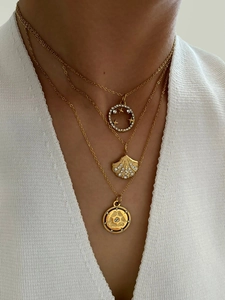 Close-up of layered gold necklaces with shell pendant and coin charm on a female model