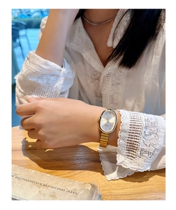 Close-up of a gold oval quartz watch with a metal link strap on a woman wrist