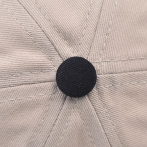 Close-up of beige cotton twill baseball cap crown with black top button and stitching
