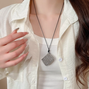 Close-up of hollow silver diamond-shaped pendant on black cord for minimalist style