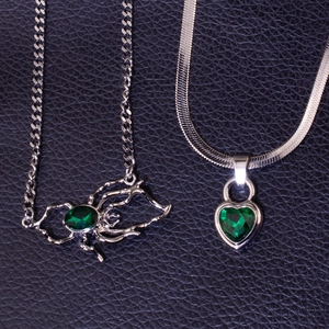 Close-up of emerald green spider and heart pendants with silver cuban and snake chains