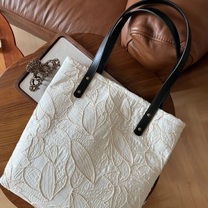 Macro detail of ivory tote bag featuring leaf embroidery and black leather strap with studs