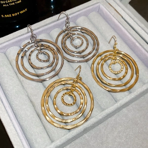 Detail of layered geometric hoop earrings in gold and silver with textured hammered finish