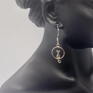 Detail view of silver cat silhouette drop earrings on a black portrait model