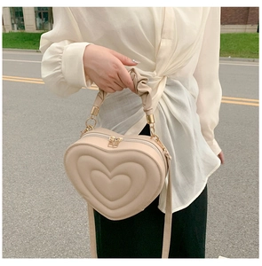 Detail of beige heart-shaped handbag with embossed patterns and ruched handle detail