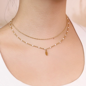 Close-up of golden double-layer necklace featuring white beads and feather pendant
