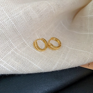 Close-up of golden square earrings with textured finish on fabric and leather backdrop