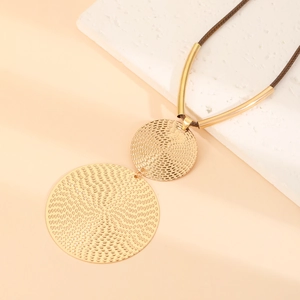 Bohemian gold textured double disc pendant necklace with brown cord on a stone prop