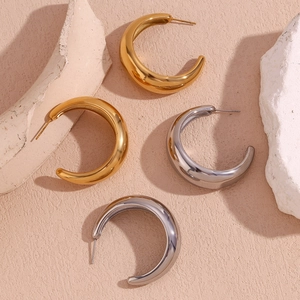 Macro detail of thick C-shaped gold and silver earrings on decorative stone background