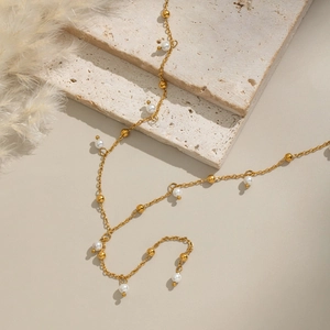 Elegante collana a catena dorata con piccole perle bianche e perline d'oro su base in pietra