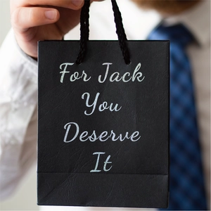 Close-up of black gift bag with silver glitter text held by a man in a business suit
