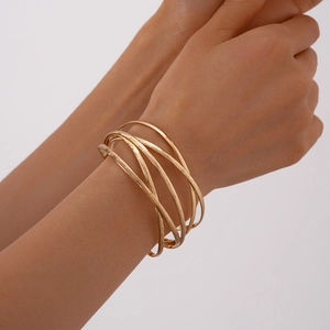 Detail shot of matte gold multi-layer crisscross bracelet worn by model on plain background