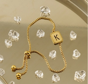 Detail of adjustable gold K-letter bracelet with frosted texture on a golden tray