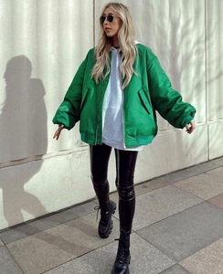 Street style shot of an oversized green bomber jacket paired with black leggings and boots