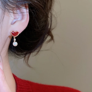 Detail of a red heart enamel earring with pearl drop worn by a model in close-up view