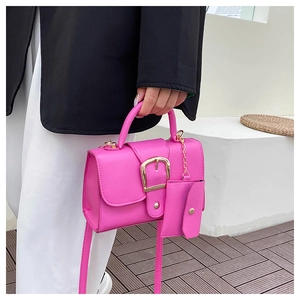 Detail view of pink crossbody bag with gold buckle, leather texture, and mini pouch charm