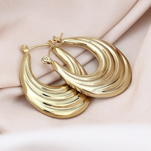 Detailed view of chunky gold hoop earrings with a wavy ridged texture on pink silk fabric