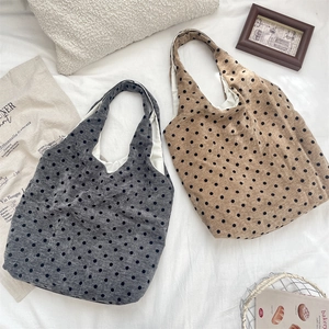 Dettaglio flat lay di borse in tela a pois grigie e kaki su un morbido letto bianco