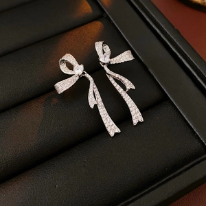 Detailed macro view of silver bow earrings with micro-pave cubic zirconia and heart stones