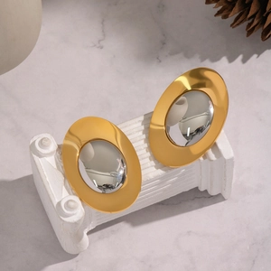 Detail of oval two-tone earrings on white stone column featuring polished gold and silver finish