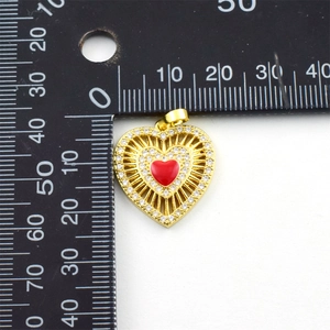 Detail view of a gold-plated red enamel heart pendant with crystals next to a ruler for size