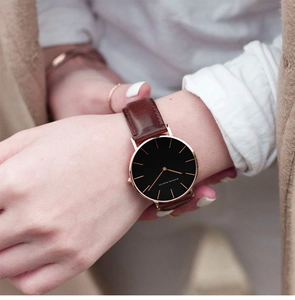 Close-up of minimalist rose gold watch with black dial and brown leather strap on wrist