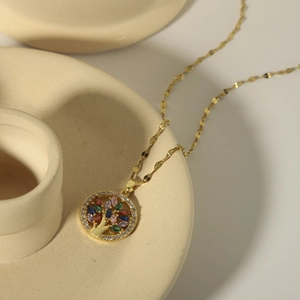 Elegant gold tree of life necklace with colorful zircons on creamy ceramic tray