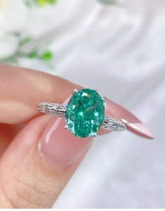Macro shot of an oval emerald gemstone set in a four-prong silver ring with pavé diamonds