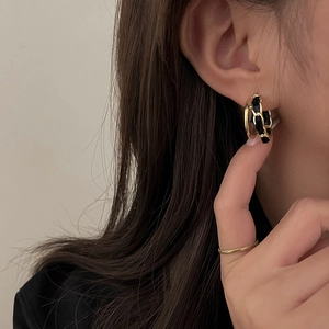 Detail of woven black fabric and gold chain geometric C-hoop earring on model