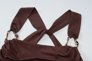 Detail of brown dress with crisscross straps and an asymmetrical gold metal buckle accent