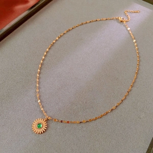 Macro shot of gold sunflower necklace featuring a green gemstone on a grey textured base