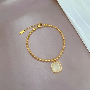 Makroaufnahme eines goldenen Titanstahl-Armbands mit einem quadratischen Katzenauge-Anhänger