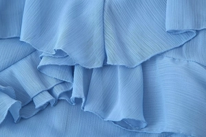 Macro shot of sky blue chiffon fabric with elegant layered ruffles and crepe texture