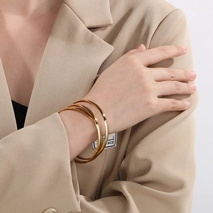Close-up of three interlocking gold titanium bangles worn with a minimalist beige suit