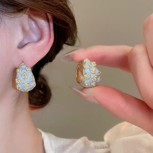 Detail of light blue enamel C-shaped earrings with gold floral patterns and rhinestones