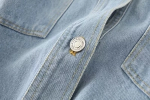 Macro shot of light blue washed denim fabric texture and engraved metal button detail